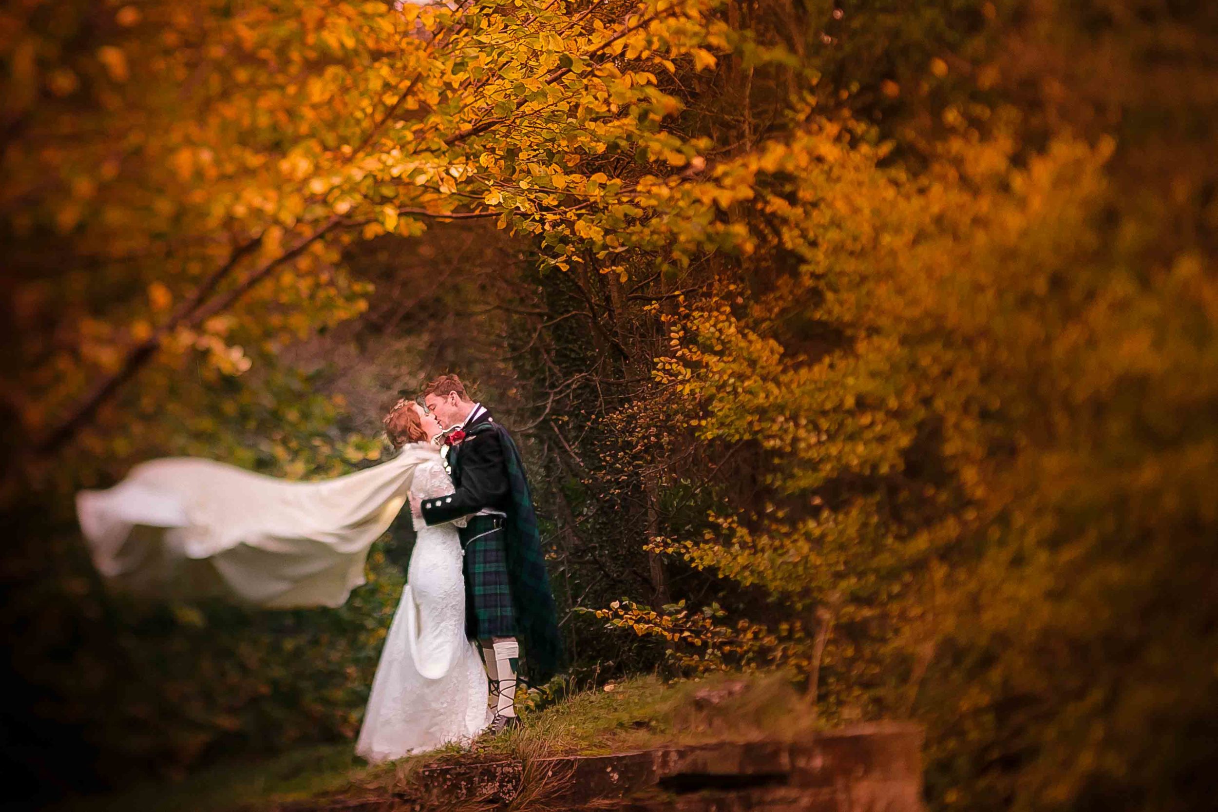 Scottish bride with flowing cape and kilted groom stand beneath orange trees.