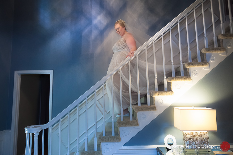 bride walking down staircase with hand on railing and train falling behind