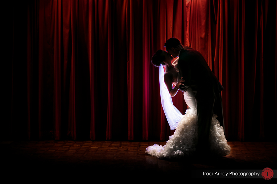 backlit bride and groom embrace against red theater curtain at lux Grandover Resort wedding in Couture Olia Zavozina Gown in Greensboro, NC