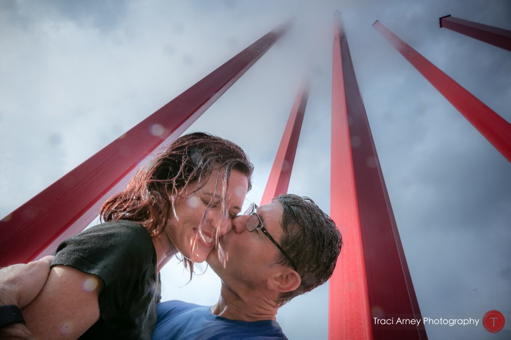 Couple kisses in mist at art structure Artivity on the Green in Winston-Salem NC during their engagement session.